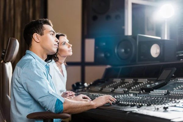 Dois músicos multiculturais que trabalham no console de mixagem em estúdio de gravação — Fotografia de Stock