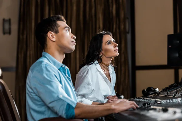 Two attentive multicultural colleagues working at mixing console in recording studio — Stock Photo