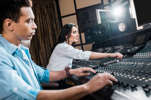 Selective focus of handsome mixed race sound producer working at mixing console near attractive colleague — Stock Photo