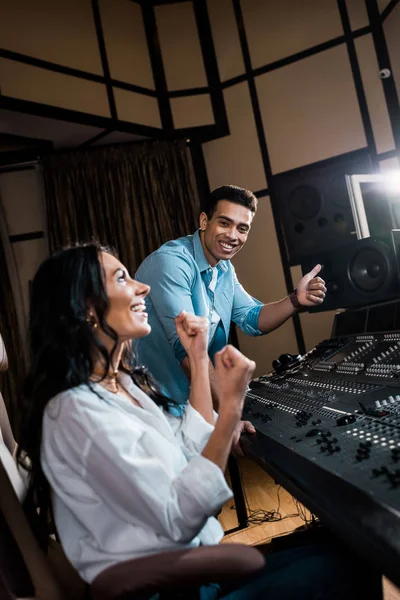 Two happy multicultural sound producers showing success gestures in recording studio — Stock Photo
