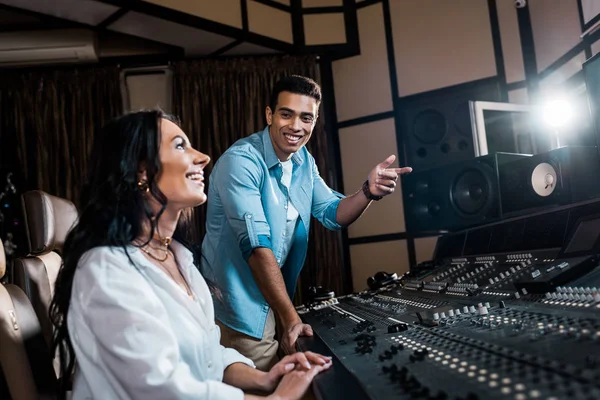 Smiling handsome sound producer pointing with finger near pretty smiling colleague — Stock Photo