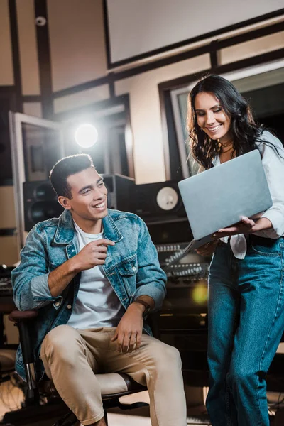 Produtores de som multicultural alegres usando laptop no estúdio de gravação — Fotografia de Stock