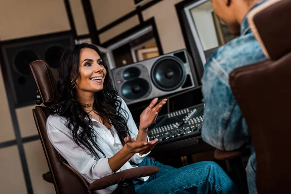 Cheerful attractive sound producer talking to mixed race colleague in recording studio — Stock Photo