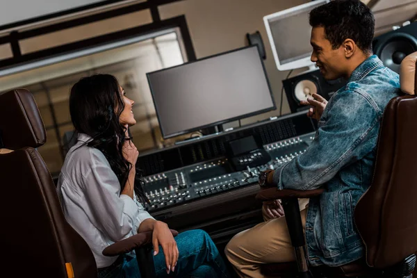 Two young smiling sound producers working sitting near mixing console while working in recording studio — Stock Photo