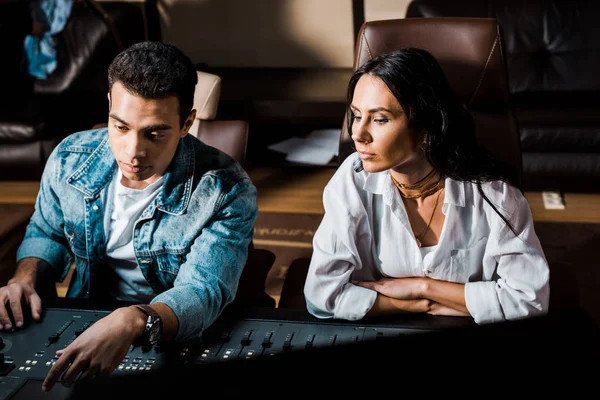 Two concentrated multicultural sound producers working at mixing console in recording studio — Stock Photo