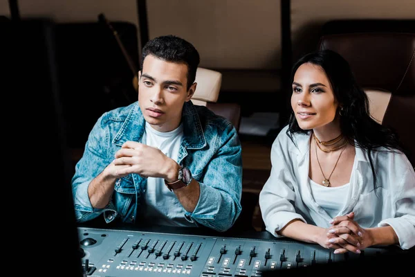 Dos productores de sonido multicultural atentos que trabajan en la consola de mezcla en el estudio de grabación - foto de stock