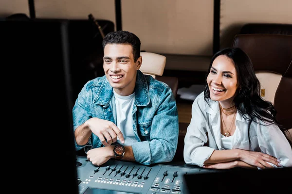 Two cheerful multicultural sound producers working at mixing console in recording studio — Stock Photo