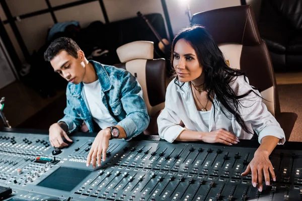 Deux jeunes producteurs sonores multiculturels attentifs travaillant sur console de mixage en studio d'enregistrement — Photo de stock