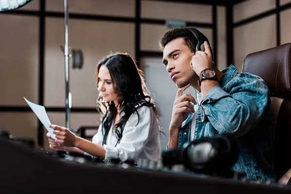 Foyer sélectif du producteur de son mixte concentré race dans les écouteurs près de joli collègue travaillant à la console de mélange — Photo de stock