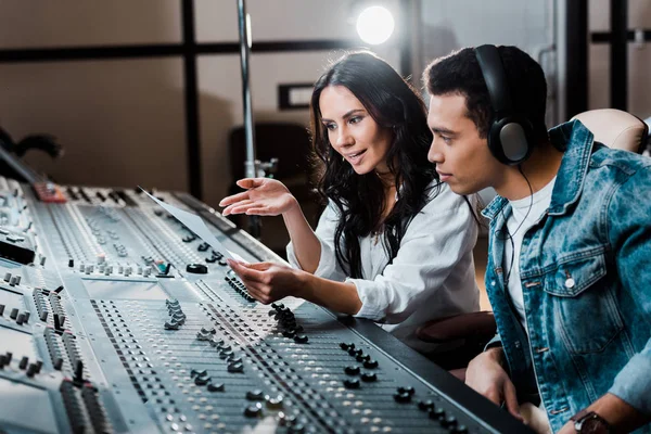 Dois jovens produtores multiculturais de som que trabalham no console de mixagem em estúdio de gravação — Fotografia de Stock