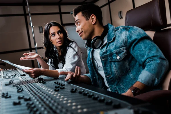 Two quarrelling multicultural sound producers working at mixing console in recording studio — Stock Photo