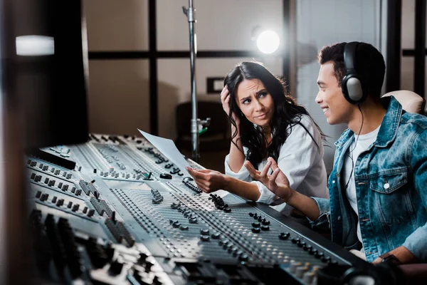 Two sound producers talking while working at mixing console in recording studio — Stock Photo