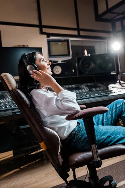 Pretty, smiling mixed raced sound producer listening music in headphones near mixing console — Stock Photo