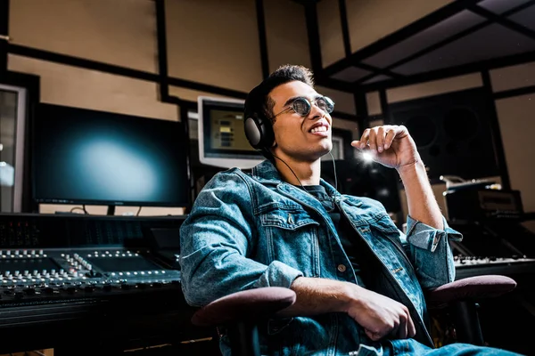 Productor de sonido mestizo y atractivo en auriculares escuchando música en un estudio de grabación - foto de stock