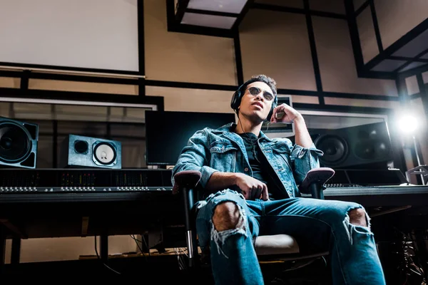 Productor de sonido de raza mixta atento en auriculares escuchando música en estudio de grabación - foto de stock