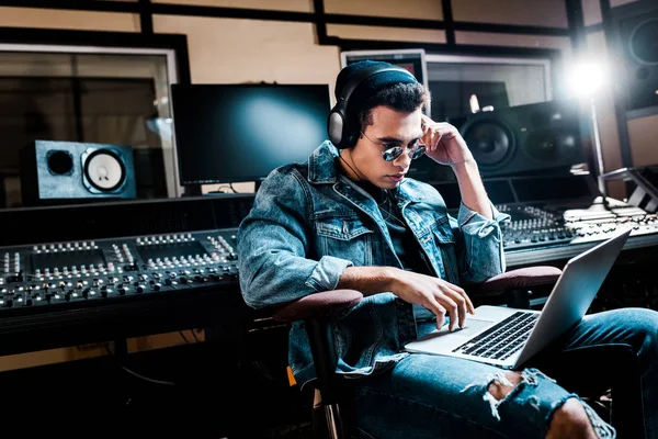 Concentrated mixed race sound producer in headphones using laptop in recording studio — Stock Photo