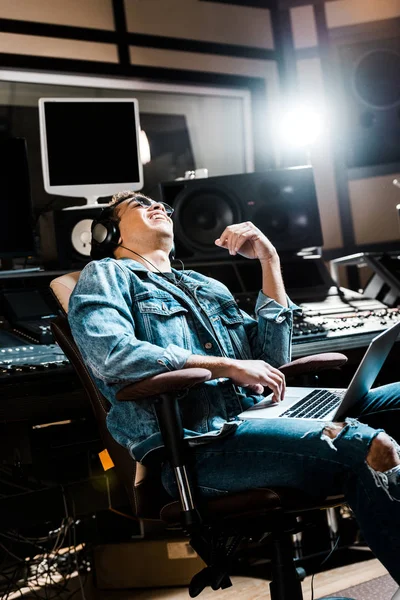 Souriant mélangé producteur sonore dans les écouteurs écouter de la musique blanche assis dans la chaise de bureau — Photo de stock