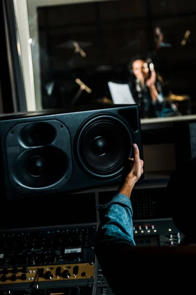 Selective focus of mixed race sound producer showing thumb up to woman singing in recording studio — Stock Photo