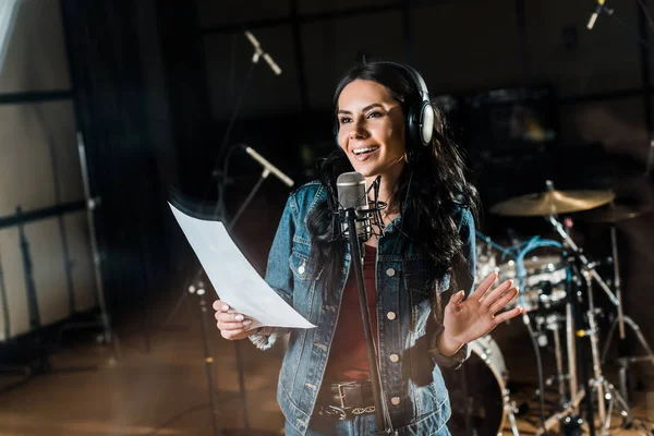 Selective focus of smiling woman singing in recording studio near microphone — Stock Photo
