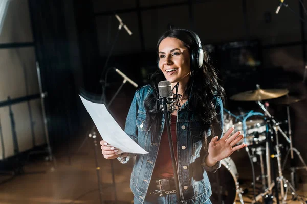 Enfoque selectivo de la mujer sonriente cantando en el estudio de grabación cerca del micrófono — Stock Photo