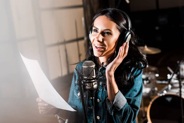 Foyer sélectif de belle femme souriante dans les écouteurs chantant en studio d'enregistrement — Photo de stock