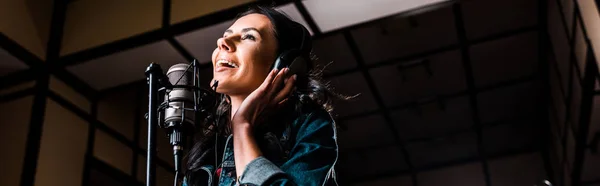 Panoramic shot of beautiful inspired woman singing near microphone in recording studio — Stock Photo