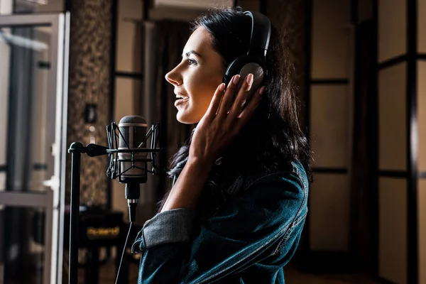 Side view of beautiful woman singing near microphone in recording studio — Stock Photo