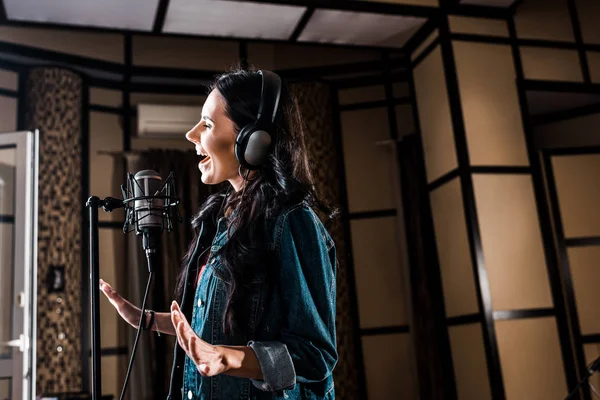 Belle femme inspirée chantant près du microphone en studio d'enregistrement — Photo de stock
