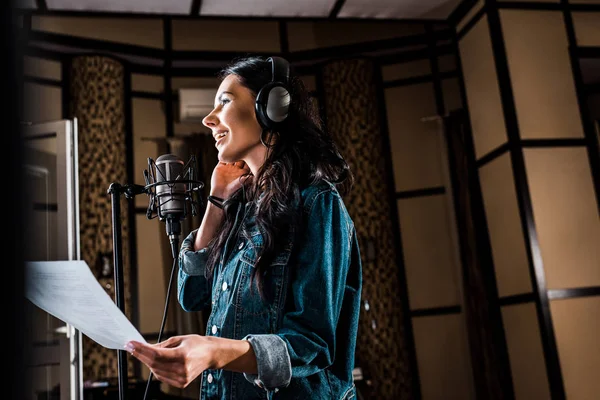Selective focus of pretty woman holding paper with text while singing in recording studio — Stock Photo