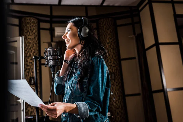 Enfoque selectivo de la mujer bonita sosteniendo papel con texto mientras canta en el estudio de grabación - foto de stock