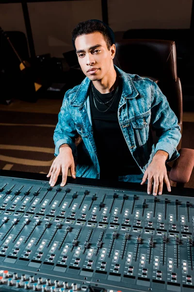Producteur sonore métissé concentré travaillant à la console de mixage en studio d'enregistrement — Photo de stock