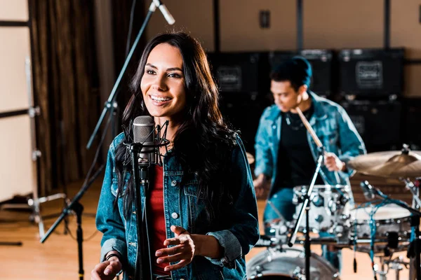 Bonita mujer cantando mientras músico de raza mixta tocando la batería en el estudio de grabación - foto de stock