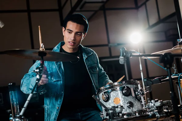 Handsome mixed race musician playing drums in dark recording studio — Stock Photo