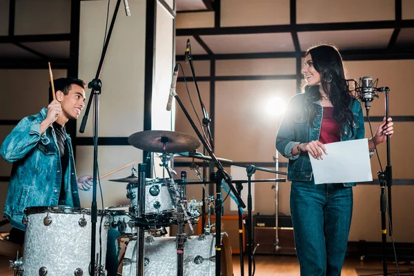 Handsome mixed race musician at drums and attractive singer near microphone in recording studio — Stock Photo