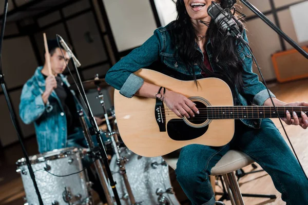 Partial view of musician playing guitar and singing while mixed race man playing drums in recording studio — Stock Photo