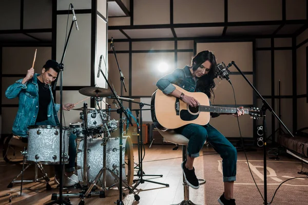 Schöne Frau spielt Gitarre, während gemischte Rassenmusiker Schlagzeug im Tonstudio spielen — Stockfoto