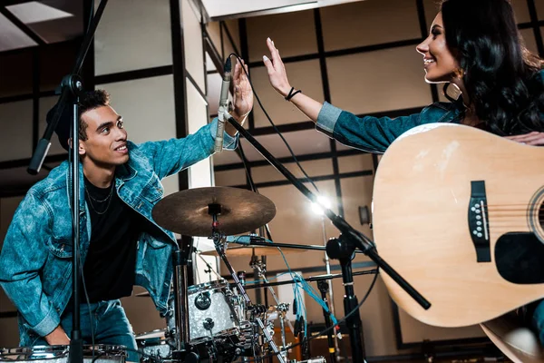 Jóvenes músicos multiculturales sonrientes dando cinco en el estudio de grabación - foto de stock