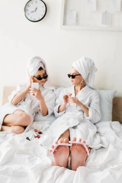 Selective focus of barefoot woman in bathrobe and sunglasses lying with pedicure in bed — Stock Photo