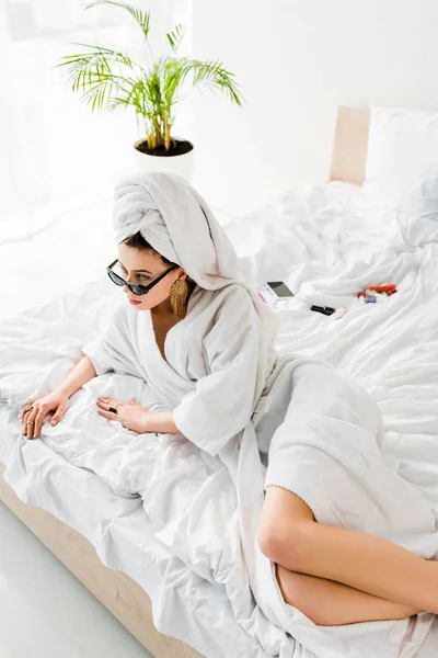 Overhead view of stylish woman in bathrobe and sunglasses lying in bed — Stock Photo
