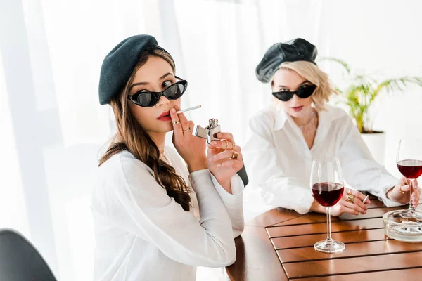 Selektiver Fokus der eleganten Frau mit schwarzer Baskenmütze und Sonnenbrille, die Zigarette in der Nähe ihres Freundes anzündet — Stockfoto