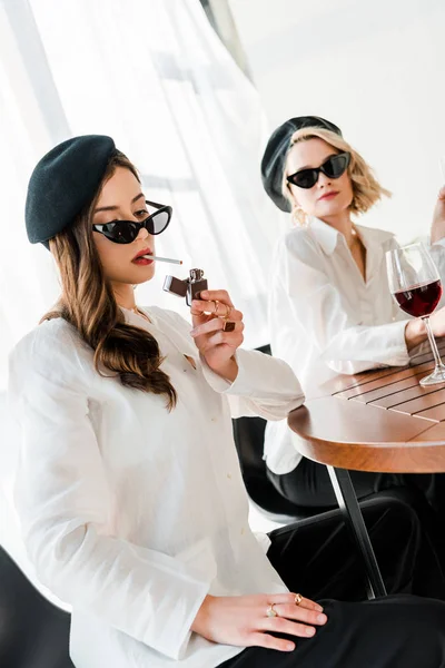 Elegante Frau mit schwarzer Baskenmütze und Sonnenbrille zündet sich Zigarette bei Freund an — Stockfoto