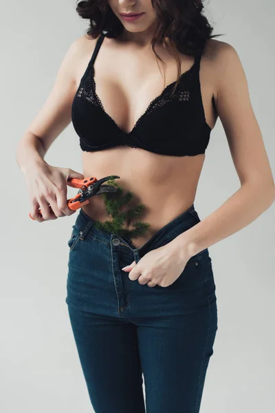 Cropped view of woman in black bra cutting plant in pants with secateurs isolated on grey — Stock Photo
