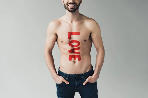 Vista recortada del hombre sin camisa con inscripción en el cuerpo de pie con las manos en los bolsillos en gris - foto de stock