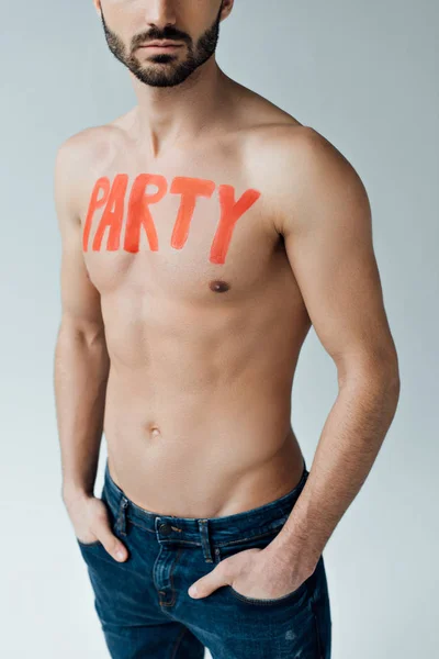 Cropped view of shirtless man with inscription on body standing with hands in pockets isolated on grey — Stock Photo