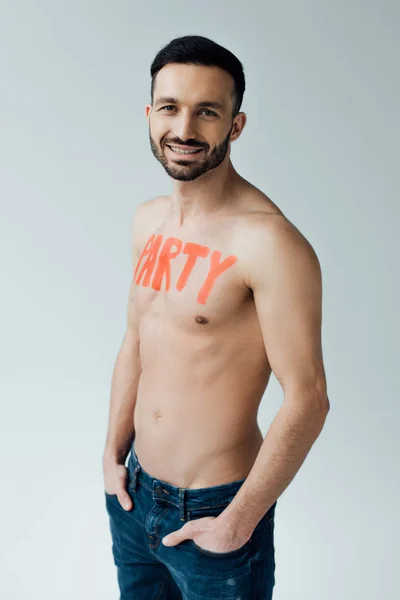 Smiling shirtless man with inscription on body with hands in pockets isolated on grey — Stock Photo