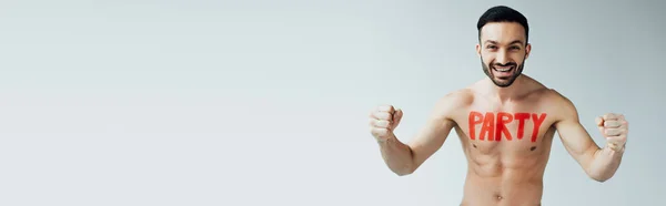 Panoramic shot of smiling shirtless man with inscription on body showing yes gesture on grey — Stock Photo