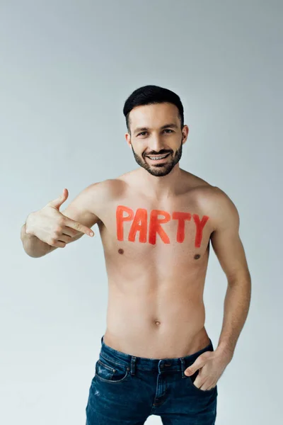 Laughing shirtless man with inscription on body pointing with finger on grey — Stock Photo