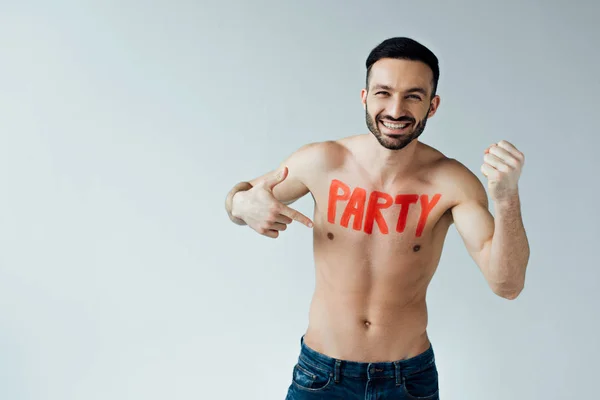 Uomo senza camicia ridente con iscrizione sul corpo che punta con il dito sul grigio — Foto stock