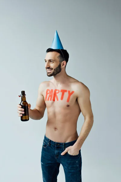 Человек в кепке для вечеринок держит пиво и смотрит в сторону, изолированный от серого — стоковое фото