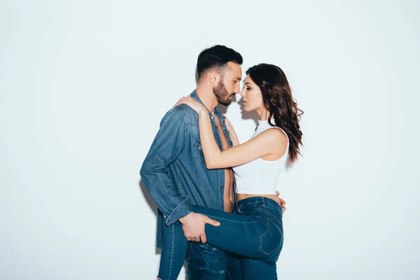 Sensual loving couple in jeans embracing on grey — Stock Photo